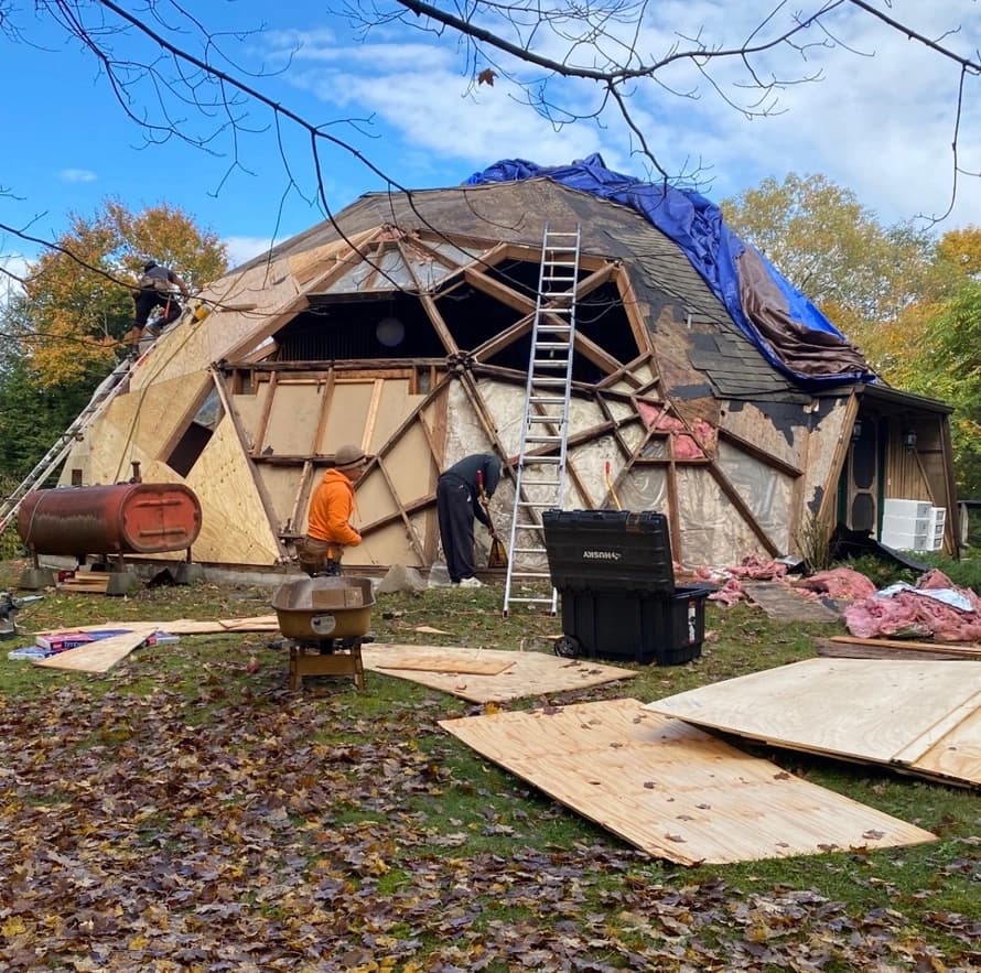 Workers renovating a geodesic dome roof with premium roofing materials on wooded residential site